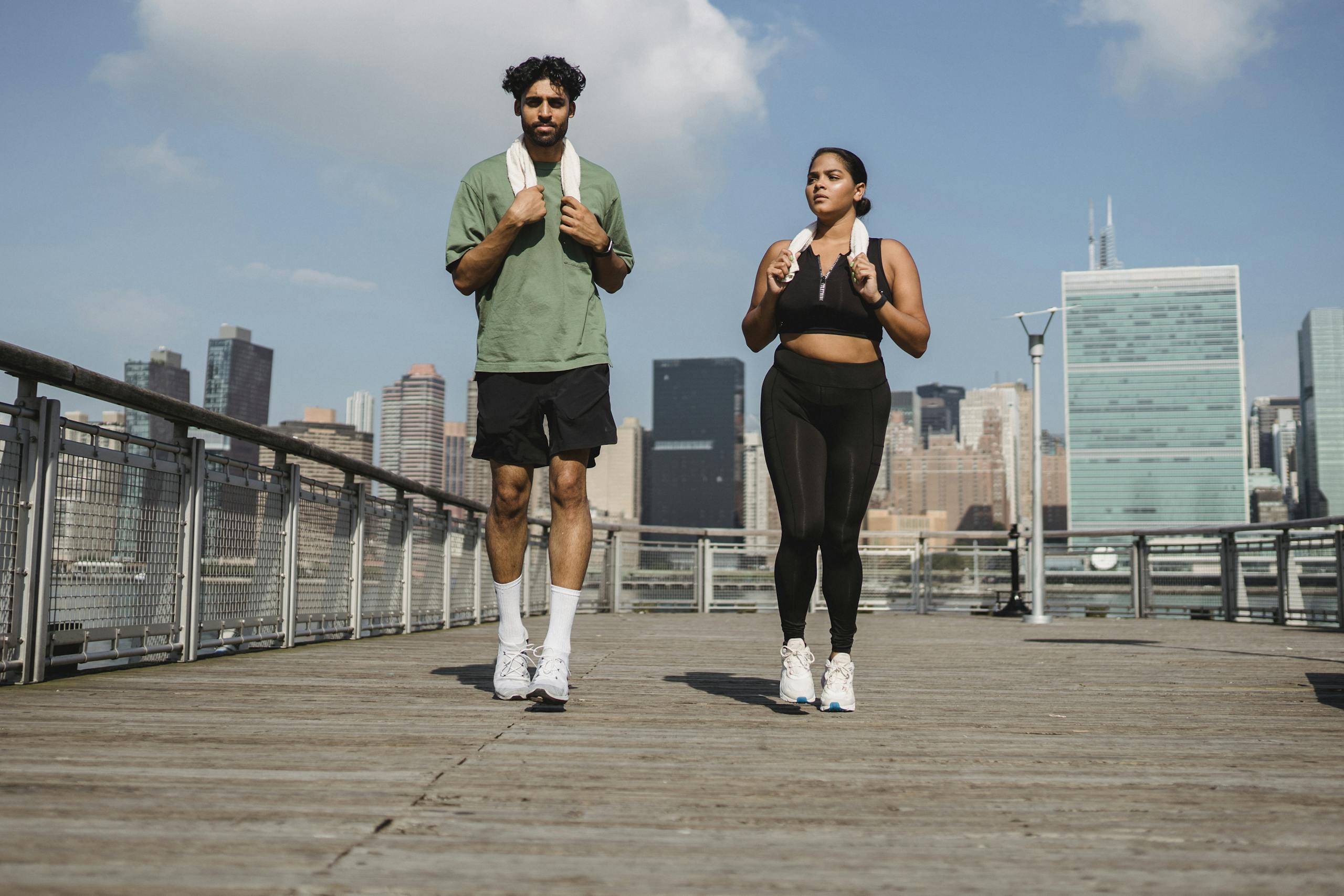 A couple jogging on a city boardwalk with a modern skyline in the background.