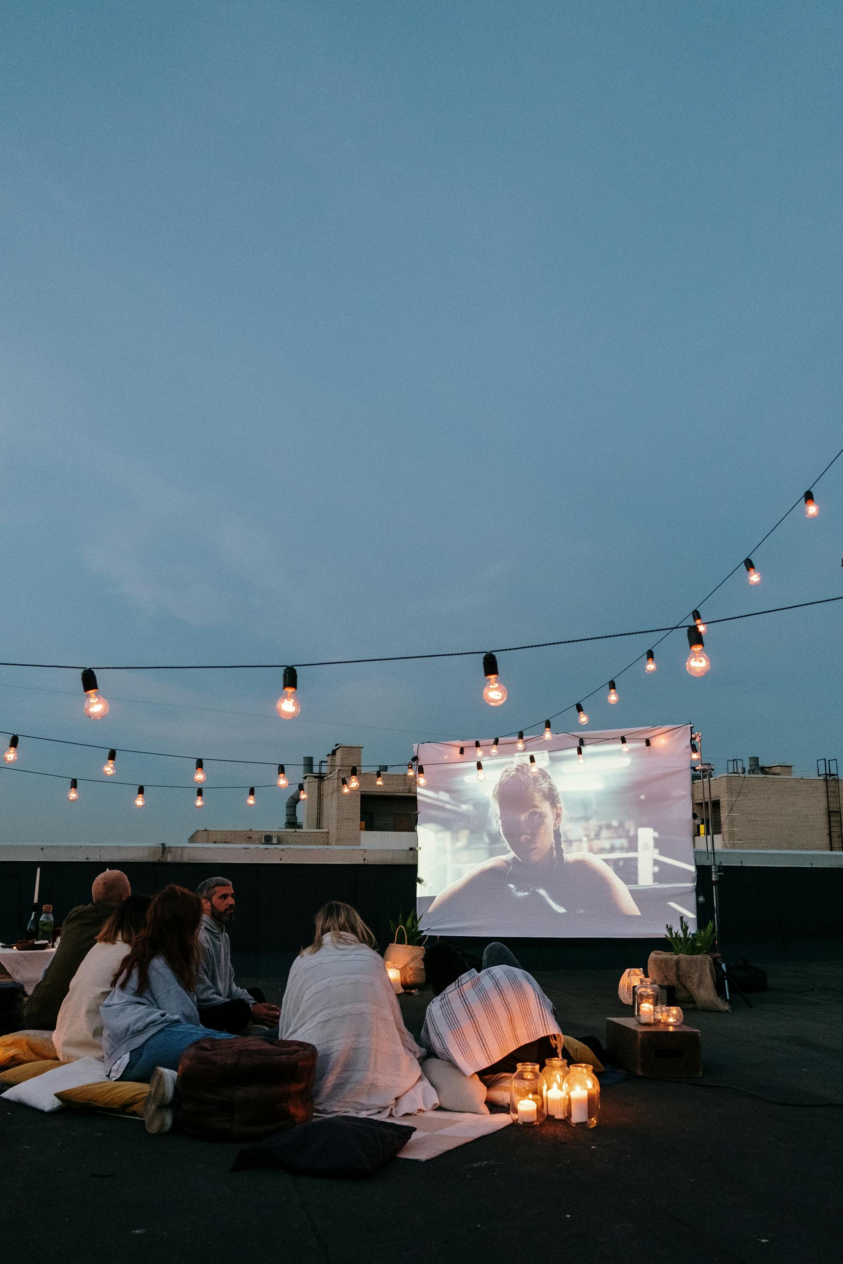 Group of friends enjoying a cozy rooftop movie night with string lights.